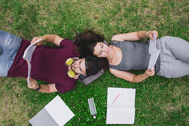 Two students are laying on the gras while studying.