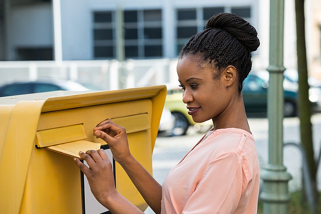 A young woman is inserting a letter into a letter box.
