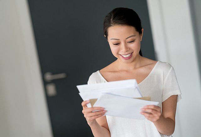 A young, smiling woman is reading a letter.